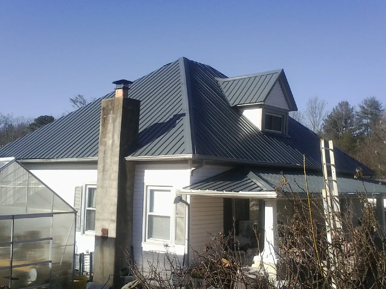 Dark blue standing seam metal roof on a white farmhouse with dormer — Slate & Tile Roof Repair by Roofing Brothers in Lebeau
