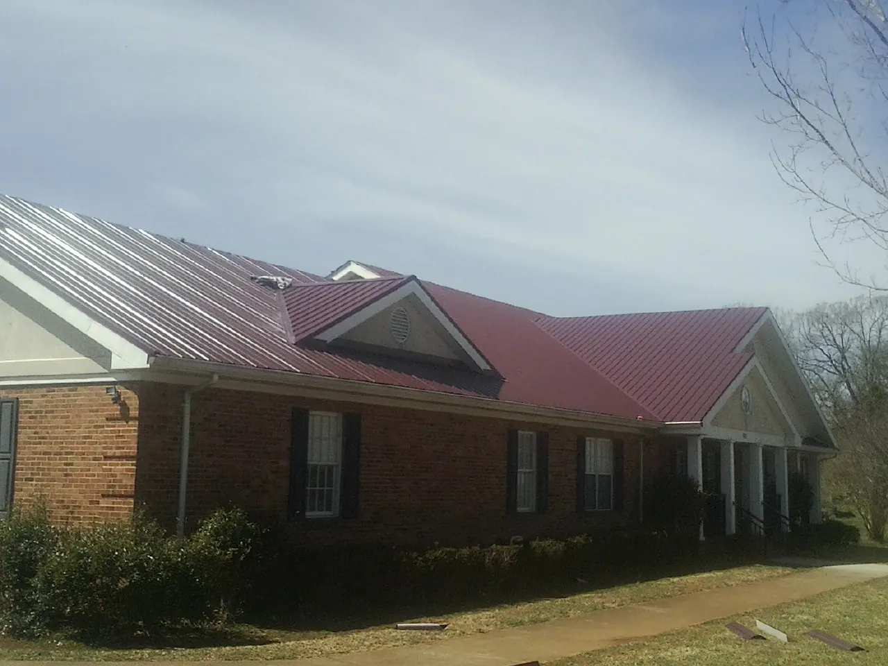 Red metal roof with gabled entries on a long brick building, from a Hail Damage Roof Repair job in Lebeau