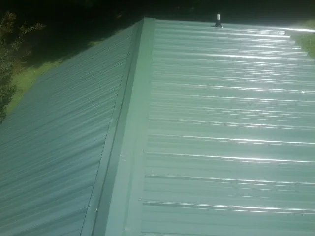 New green metal panels meeting at the ridge of a roof — Flat Roof Repair work by our crew in Lebeau