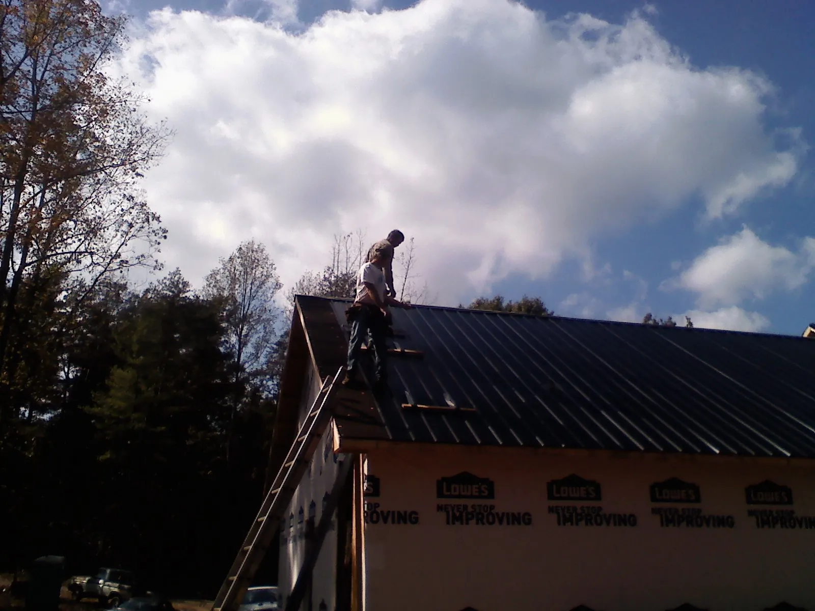 Roofer fastening dark metal panels high against a cloudy sky, from a Roof Inspection job in Lebeau