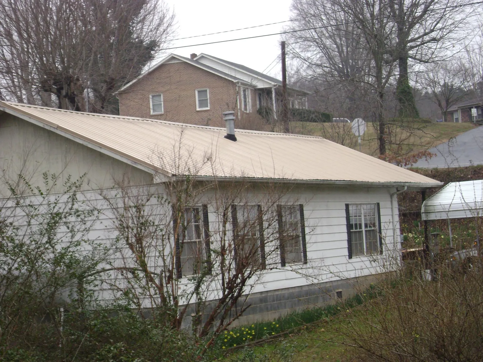 Tan metal roof on a white sided house set into a hillside — Commercial Roofing by Roofing Brothers in Lebeau