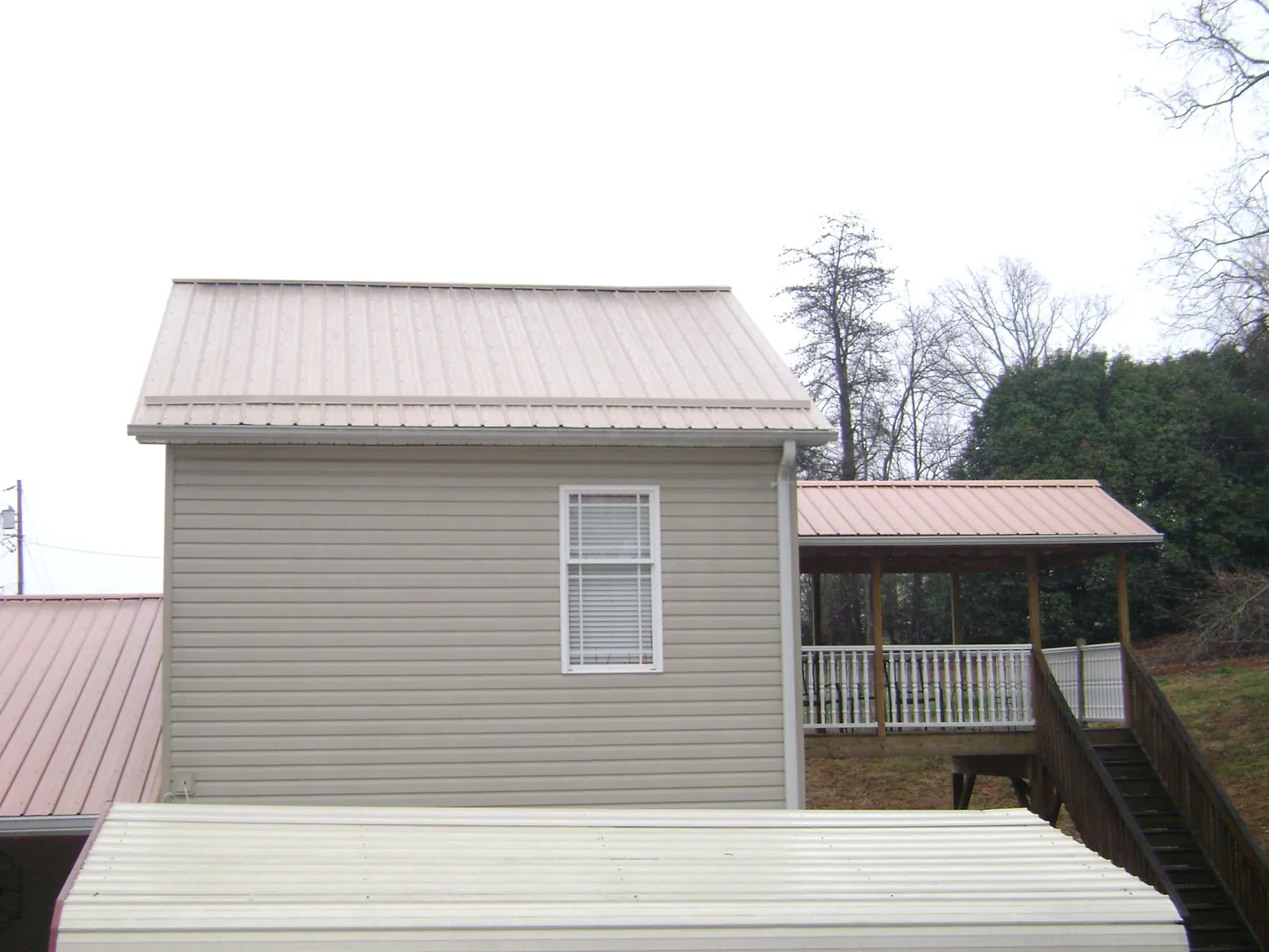 Tan metal roofs on a two story addition and attached porch, from a Roof Replacement job in Lebeau